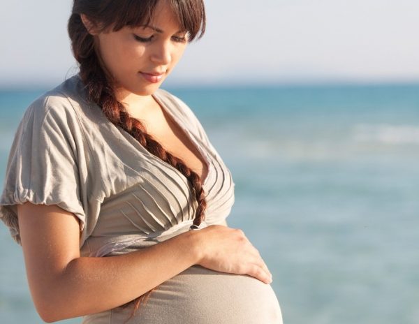 Беременная девушка с косичкой на фоне моря