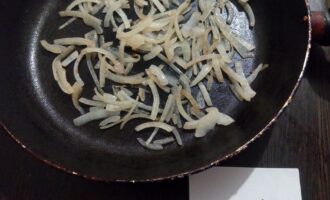 Шаг 3: Пока баклажаны пекутся, почистите лук и порежьте его полукольцами. Нагрейте сковороду с одной ложкой оливкового масла и обжарьте лук на слабом огне пару минут.